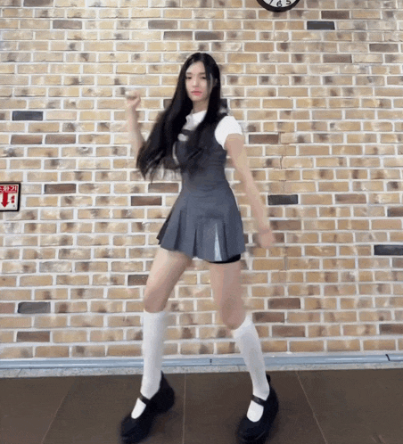 a girl in a gray dress and white socks is dancing in front of a brick wall ..
