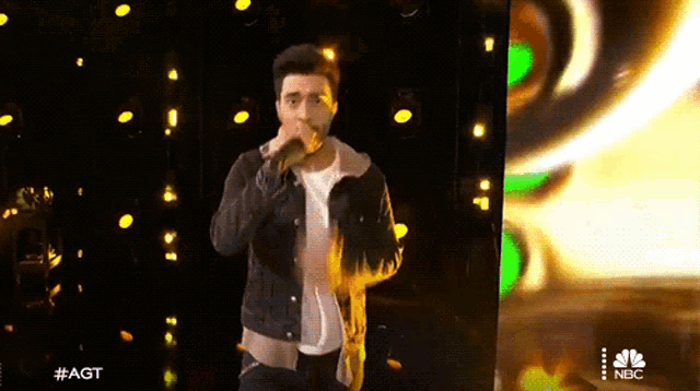 a man singing into a microphone with a nbc logo in the corner