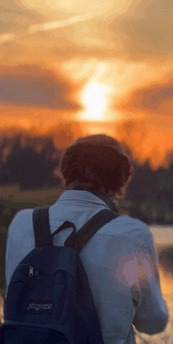 a person wearing a black jansport backpack looks at the sunset