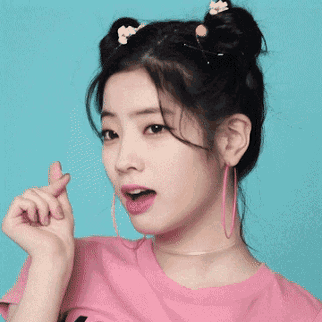 a woman wearing a pink shirt and pink hoop earrings is making a heart shape with her hand