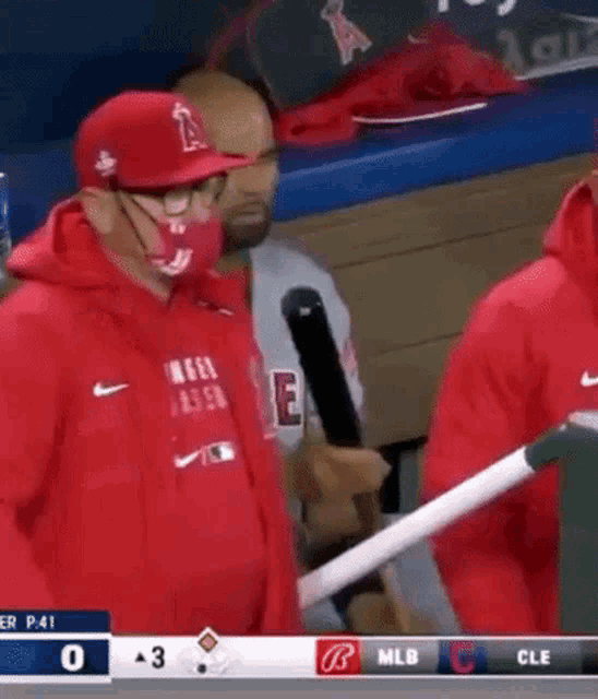 a baseball player is holding a bat in a dugout while wearing a mask .