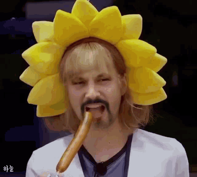 a man with a beard wearing a sunflower headband is eating a hot dog
