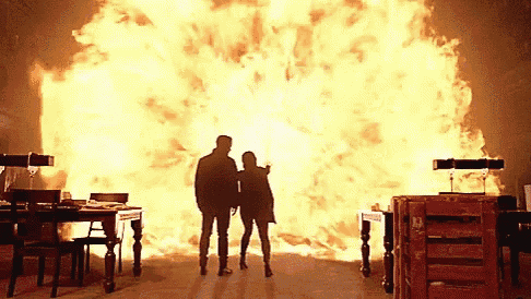 a man and a woman are standing in front of a large explosion .