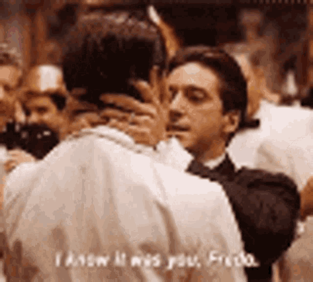 a man in a tuxedo is kissing another man in a crowded room .