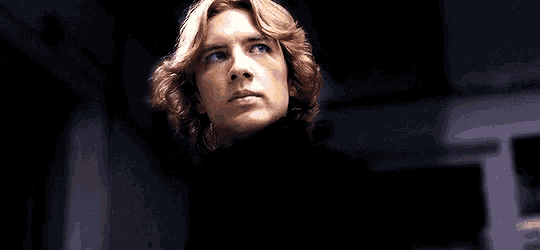 a man with blonde hair is wearing a black turtleneck sweater and looking at the camera .
