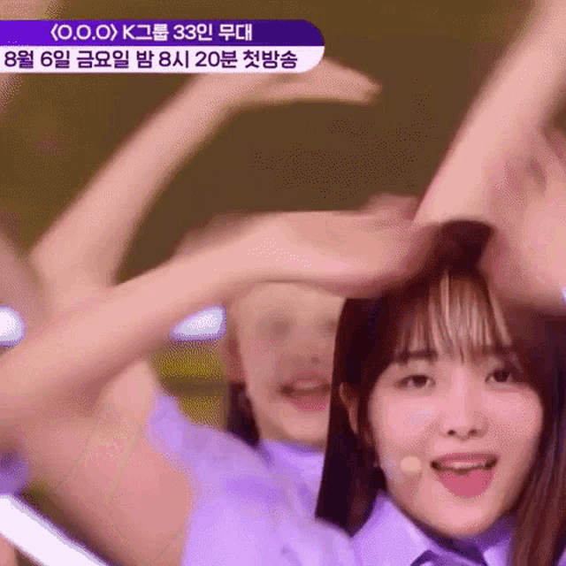 a group of girls are dancing on a stage and one of them is making a heart shape with her hands .