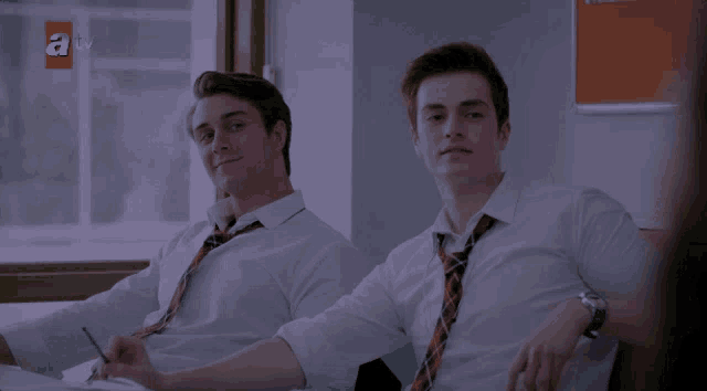 two boys sit next to each other in a classroom with a tv logo in the background