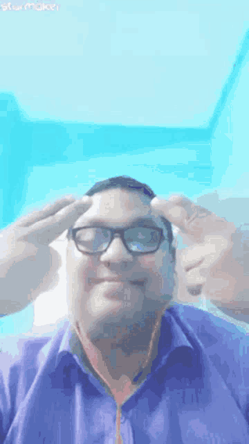 a man wearing glasses and a blue shirt is making a peace sign .