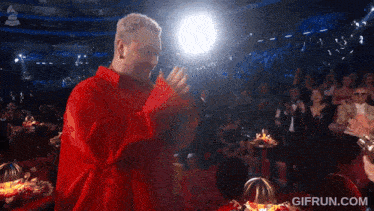 a man in a red shirt is dancing in front of a crowd with a gifrun.com watermark on the bottom
