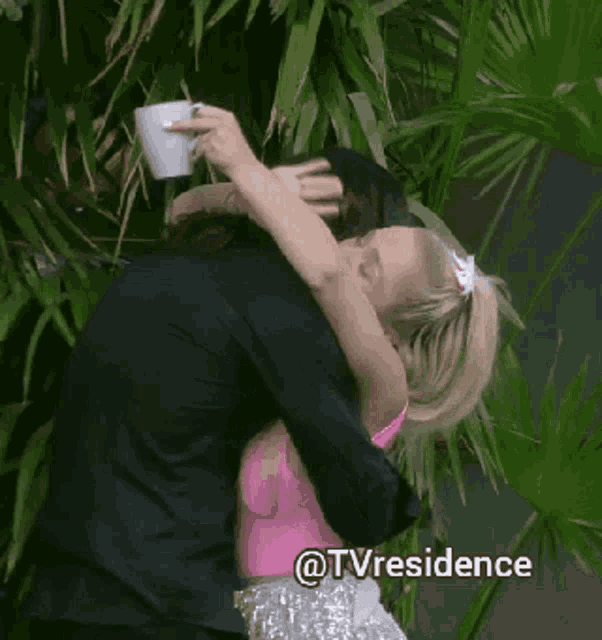 a woman in a pink top is kissing a man in a suit while holding a cup of coffee ..