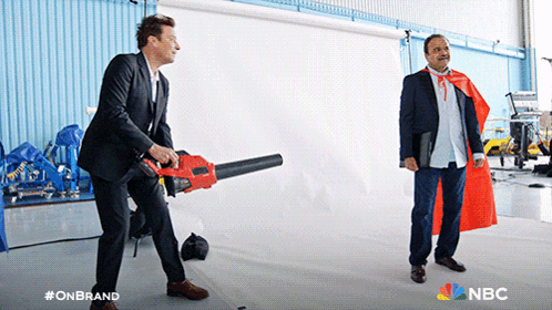 a man in a red cape is standing next to a man holding a blower