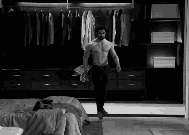 a shirtless man is standing in a closet with clothes hanging