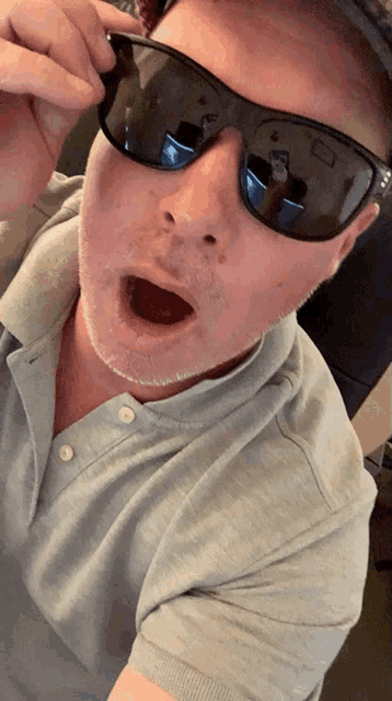 a man wearing sunglasses and a grey shirt looks surprised