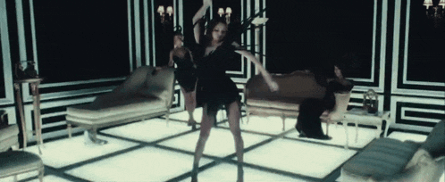 a woman in a black dress is dancing in a room with a couch