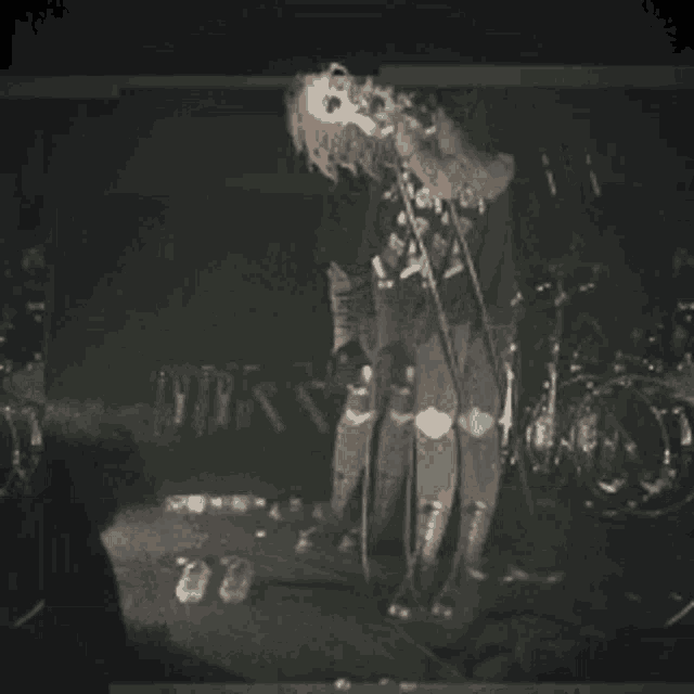 a man singing into a microphone on a stage with drums in the background