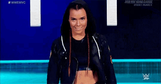 a woman in a black jacket is standing in front of a blue background and smiling .