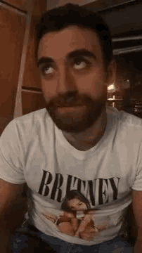 a man with a beard wearing a white t-shirt with a picture of a woman on it is looking up .