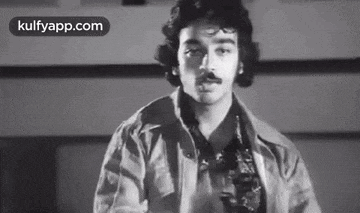 a black and white photo of a man with a mustache standing in front of a wall .