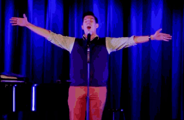 a man is standing in front of a microphone with his arms outstretched .
