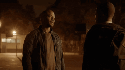 two men are standing next to each other and one of them has a backpack on his back .