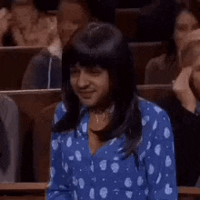a woman in a blue polka dot shirt is sitting in a classroom with other people .