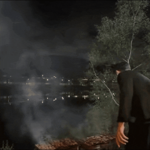 a man in a black jacket is standing in front of a grill at night