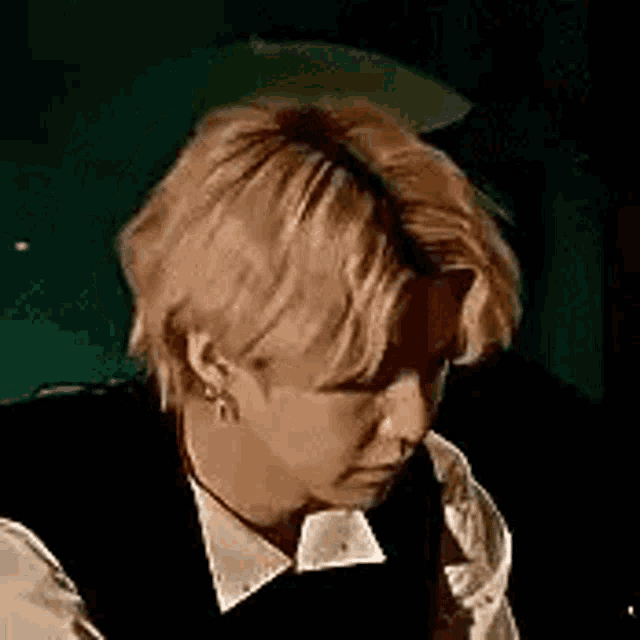 a close up of a man with blonde hair wearing a black vest and white shirt .