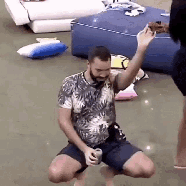 a man is kneeling down on the floor holding a can of soda .