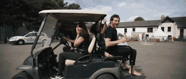 a group of people are riding in a golf cart with a police car parked in the background