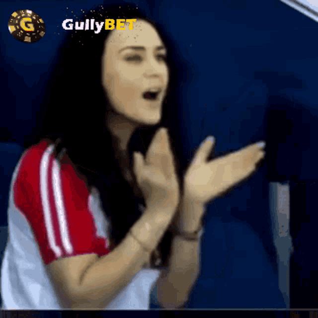 a woman in a red and white shirt is clapping in front of a gullybet logo