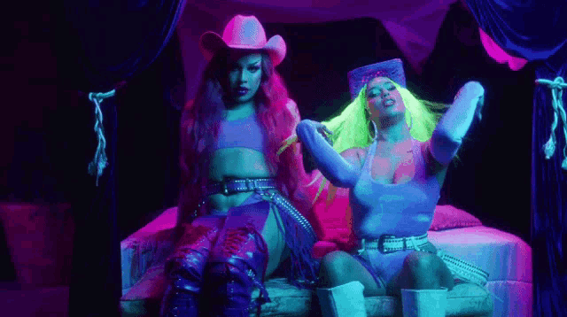 two women in cowboy hats are sitting on a bed in a room .