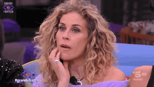 a woman with curly hair is sitting in front of a screen that says grande fratello on it