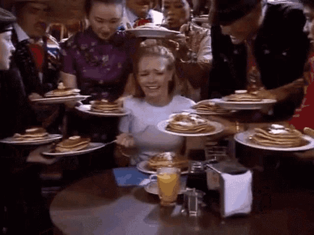 a woman sitting at a table with plates of pancakes on it .