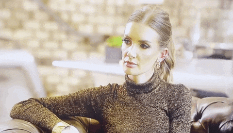 a woman is sitting on a couch wearing a turtleneck and earrings .
