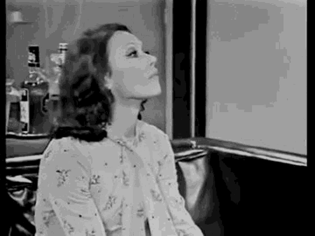 a black and white photo of a woman sitting on a couch looking up at the sky .