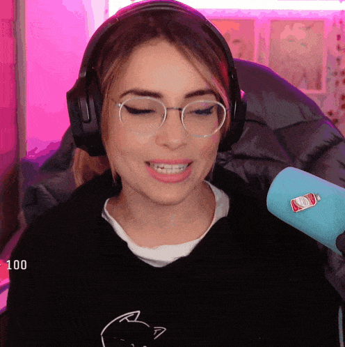 a woman wearing headphones and glasses is smiling in front of a microphone that has a bottle of ketchup on it