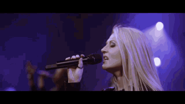 a woman singing into a microphone in front of a blue background