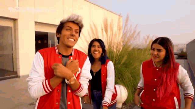 a man in a red and white varsity jacket stands with two women