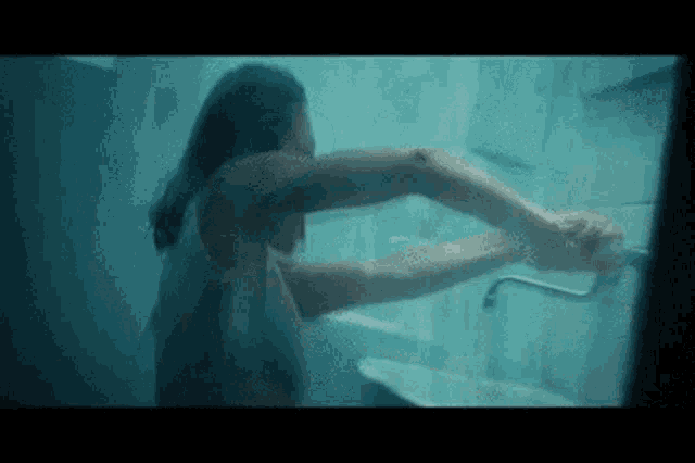 a woman is taking a shower in a bathroom while holding a faucet .