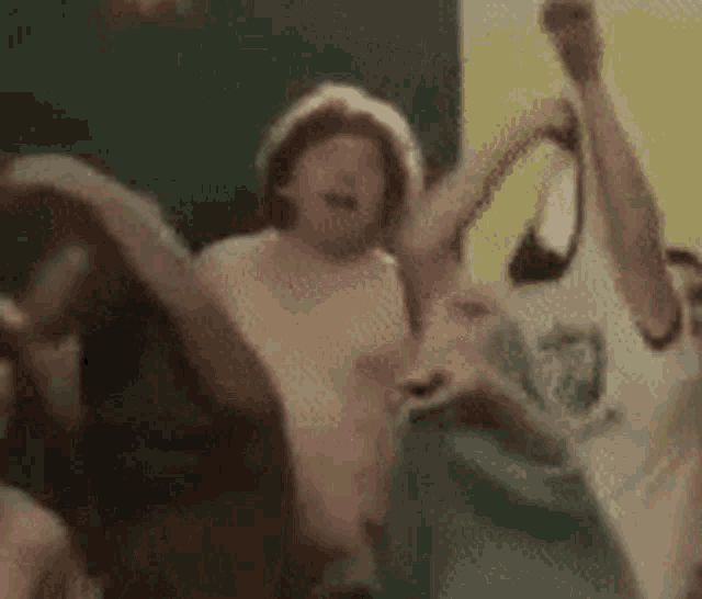 a group of people are dancing in a room with their arms in the air and a woman is holding a mirror .
