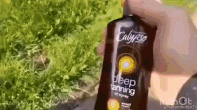 a person holding a bottle of calypso deep tanning oil spray