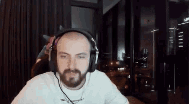 a man with a beard wearing headphones is sitting in front of a computer screen .