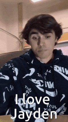 a young man wearing a hoodie is sitting at a table and making a face .
