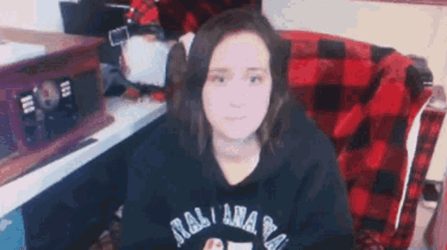 a woman in a black hoodie is sitting in a chair with a plaid blanket on the back .