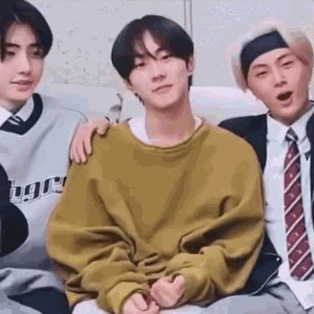 a group of young men are sitting on a couch and one of them is wearing a yellow sweater .