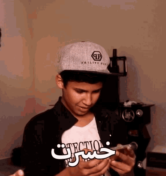 a boy wearing a hat that says philipp plein looks at his phone