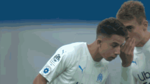 two soccer players are whispering into each other 's ears while wearing puma jerseys