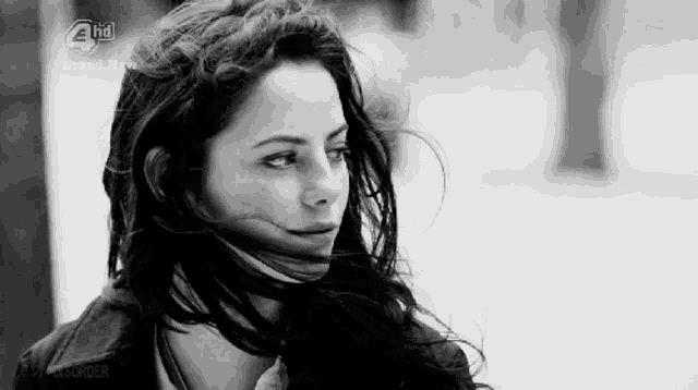 a woman with her hair blowing in the wind is standing in a black and white photo .