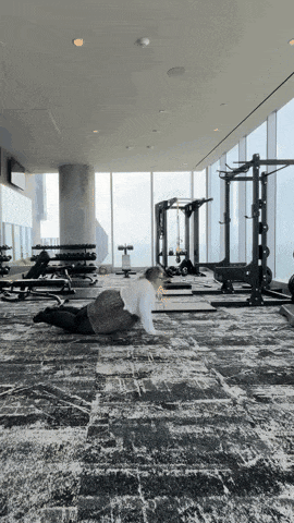 a woman is doing push ups in a gym with a lot of windows