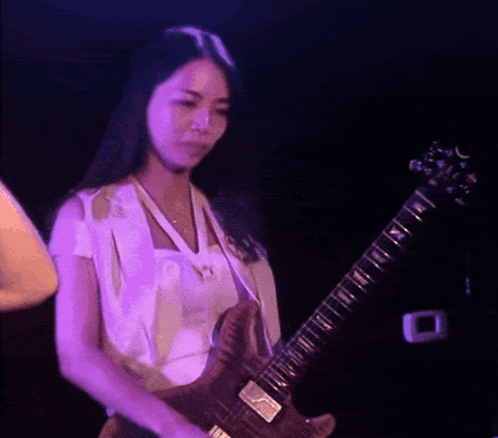 a woman is playing a guitar in a dark room with purple lights